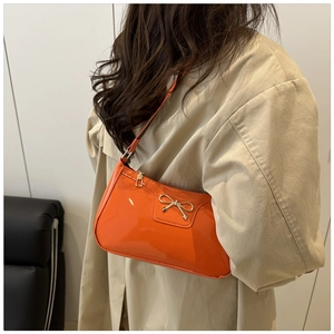 Detail of glossy orange underarm bag with golden bow and premium patent leather finish