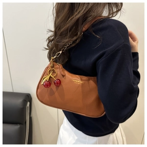 Detail of brown lychee leather crossbody bag with gold chain and cherry pendant