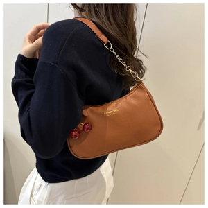 Close-up of caramel brown leather handbag with gold chain strap and cherry charm detail