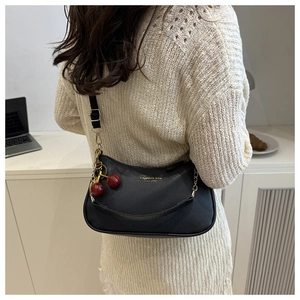 Detail of black lychee grain leather underarm bag with red cherry charm and gold buckle