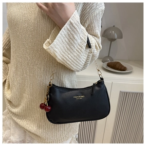 Detail of black pebbled leather handbag with gold chain and red cherry pendant charm