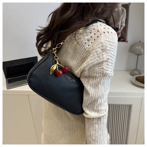 Détail du sac en cuir grainé noir avec chaîne dorée et pendentif cerise élégant