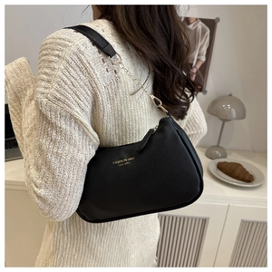 Detail of black lychee texture leather shoulder bag with golden chain strap on a model