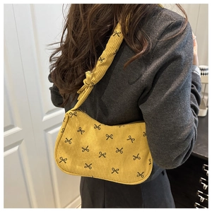 Model wearing yellow corduroy hobo bag with black bow print and knotted shoulder strap