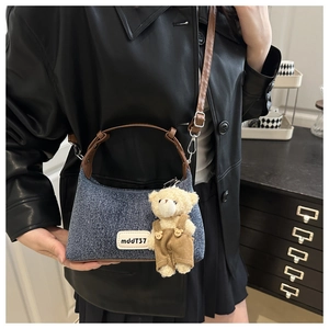 Close-up of blue denim bag with brown leather straps and a small teddy bear charm