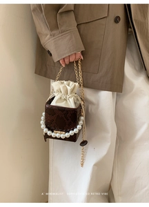 Detail of brown crocodile pattern bucket bag featuring pearl handle and gold chain strap