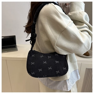 Detail of black corduroy underarm bag featuring white bow patterns and knotted strap