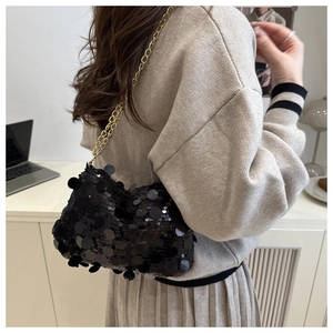 Detail of black sequin shoulder bag with gold chain strap on a model outfit
