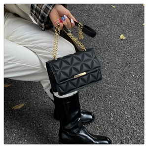 Close-up of black quilted shoulder bag with gold chain strap and square metal clasp