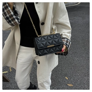 Detail of black quilted crossbody bag with gold chain and metal lock on trench coat