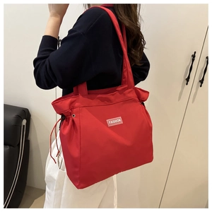 Detail of red oversized tote bag with side drawstrings and fashion label on the shoulder