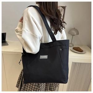 Detail of black nylon tote bag featuring fashion label and side drawstring detail