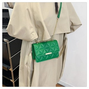 Detail of green quilted crossbody bag with gold chain strap and metal trim on beige coat