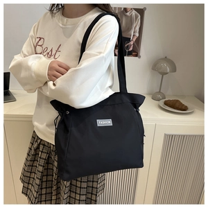 Detail of black nylon tote bag with drawstring and fashion label worn by a model