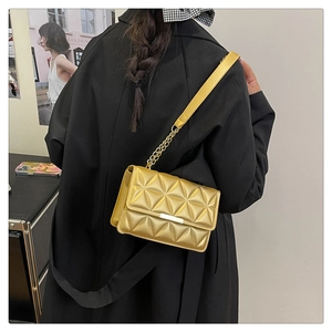 Detail of gold quilted shoulder bag with chain strap and triangular stitching texture