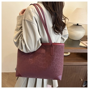 Detail of burgundy leopard print tote bag featuring leather logo tag and shoulder straps