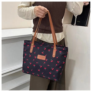 Detail of red cherry print on black tote bag with brown leather handles and brand tag