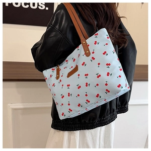 Close-up of light blue cherry print tote bag with brown leather straps worn by a model