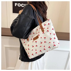 Detail of red cherry print on white canvas tote bag with brown leather handles