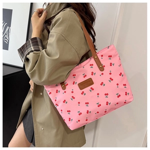 Detail view of pink fabric tote bag with red cherry prints and brown leather logo patch