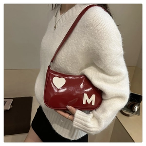 Close-up of red patent leather shoulder bag featuring heart patch and letter M detail