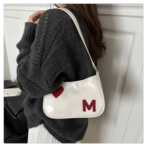 Detail of white glossy underarm bag with red heart and M letter worn with grey sweater