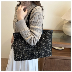 Detail of tweed tote bag with black and gold weave and elegant leather strap on a model