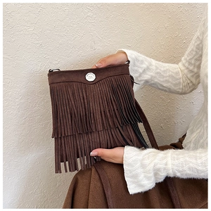 Detail of dark brown faux suede crossbody bag with long tassels and silver metal buckle