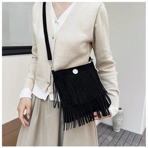 Detail shot of black faux suede crossbody bag featuring tiered long fringe and silver buckle