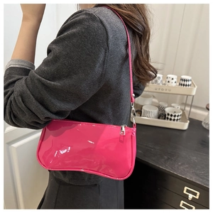 Detail view of a rose red patent leather shoulder bag worn by a model in a minimalist setting