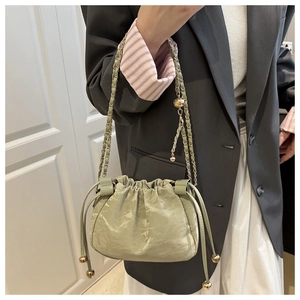 Détail d'un sac seau plissé vert clair avec bandoulière en chaîne dorée sur mannequin