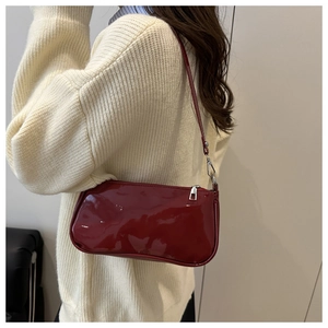 Deep red patent leather underarm bag with silver hardware on model in knit sweater