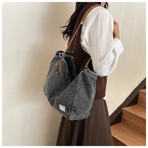 Detail of washed charcoal denim tote bag featuring brown woven strap and metallic hardware