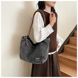 Denim tote bag with brown woven rope handle and metal plaque shown on a shoulder