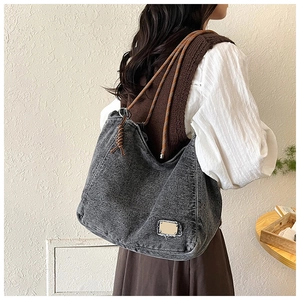 Detail of black washed denim tote bag with brown braided rope handles and gold plaque