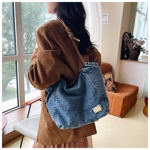 Detail of blue denim tote bag with brown woven rope strap and elegant knot design