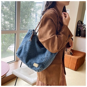 Detail of blue denim hobo bag with woven rope strap and frayed metal brand tag