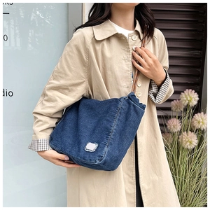 Detail of vintage denim tote bag with light patch and woven shoulder strap on model
