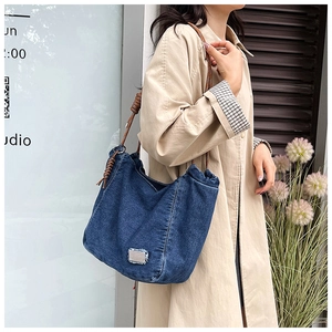Detail of blue denim tote bag with brown rope shoulder strap and silver metal plate logo