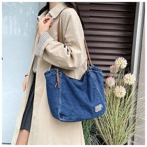 Detail of blue denim tote bag with brown braided rope handle worn by a model