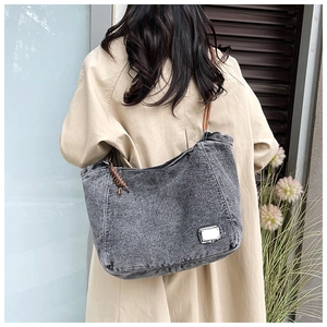 Detail view of washed grey denim tote bag with brown cord handle and vintage metal label