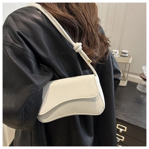 Detail view of the asymmetric curved flap and knotted shoulder strap of a beige bag