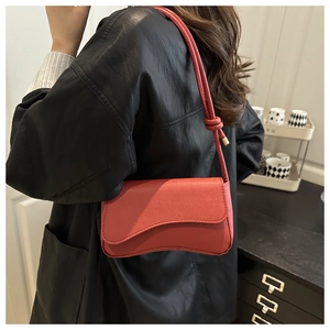 Detail of red crossbody bag with curved silhouette and unique knotted strap on a model