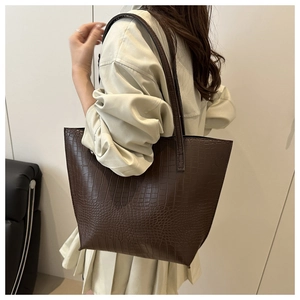 Detail view of a large brown crocodile-embossed tote bag worn over the shoulder
