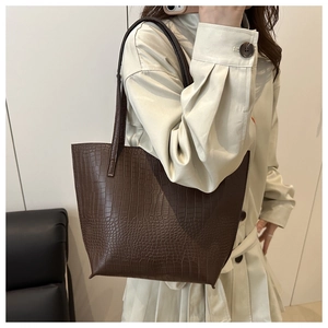 Close-up of deep brown crocodile embossed tote bag worn with a stylish trench coat