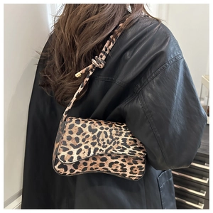 Dettaglio borsa a spalla in pelle leopardata marrone con ciondolo in metallo dorato su tracolla