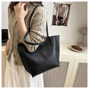 Detail of black crocodile pattern tote bag with dual shoulder straps in a cafe setting