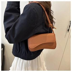 Detailed view of caramel brown leather shoulder bag with unique knot strap and gold metal tips