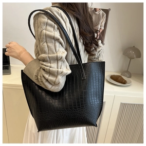 Detail of black faux leather tote bag with elegant crocodile texture and long straps
