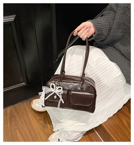 Detail of dark brown pillow bag with glossy texture, front flap pockets and lace bow charm